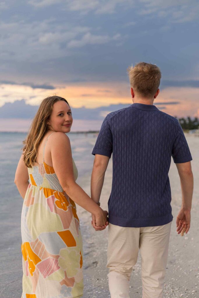 Couple walking on the beach with a blue and orange sunset behind them