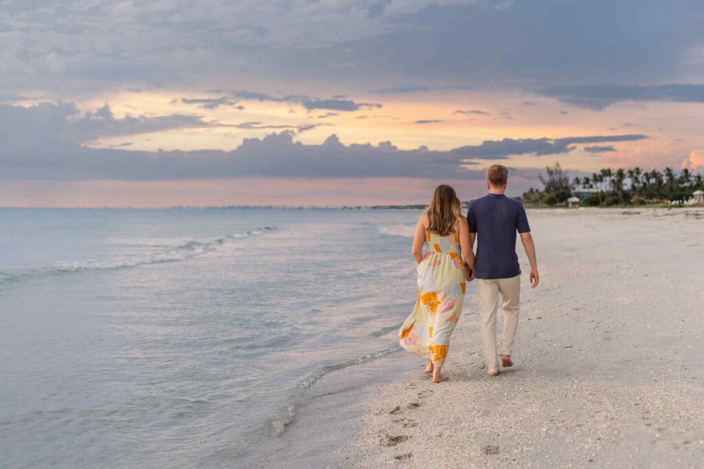 Couple walking on the beach with a blue and orange sunset behind them
