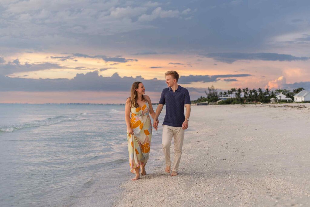 Couple walking on the beach with a blue and orange sunset behind them