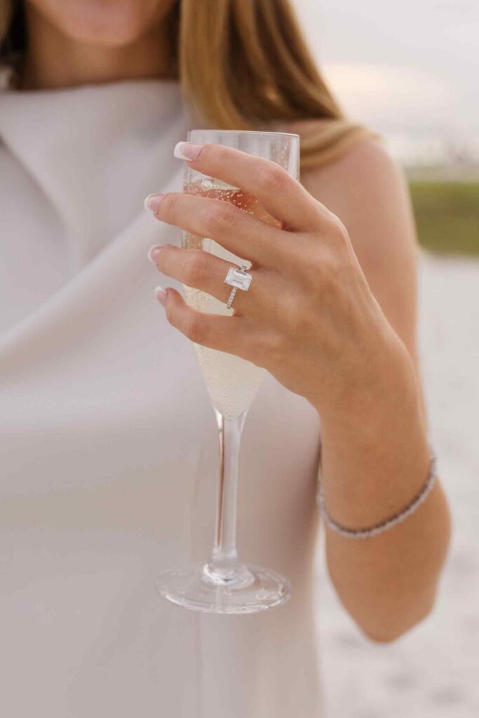 Woman holds a champagne glass with her engagement ring facing the camera