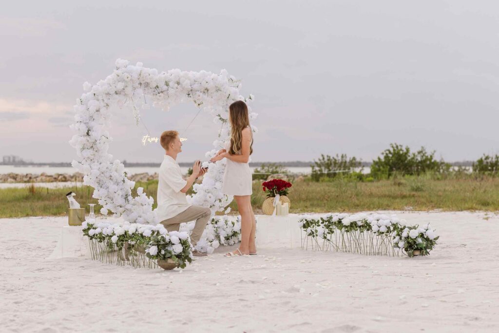 Woman and man in proposal heart arch setup on the beach